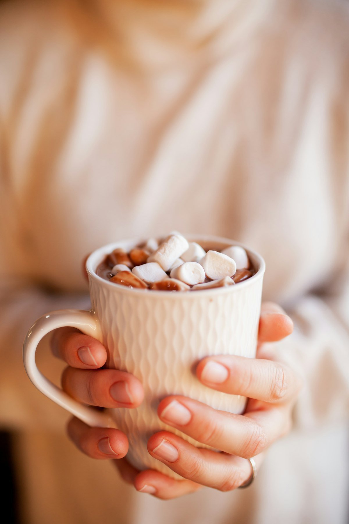 Mug of hot chocolate piled with marshmallows held in hands